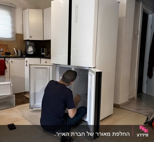 אדם מתקן מקרר עם מברגה חשמלית על הרצפה
